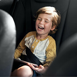 Ein Kind sitzt im Auto mit einem IPad in der Hand und lacht | Abifor