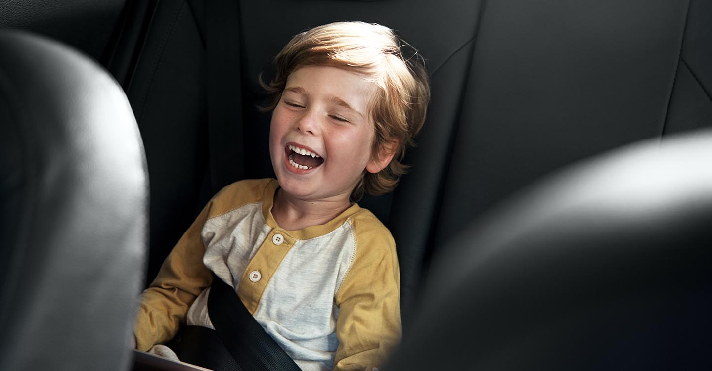 Ein Kind sitzt im Auto mit einem IPad in der Hand und lacht | Abifor